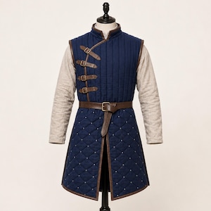 May include: A navy blue quilted vest featuring a high collar, brown leather trim, and four side-fastening buckles. The lower section displays a diamond-stitched pattern with small silver studs, secured at the waist by a brown leather belt.