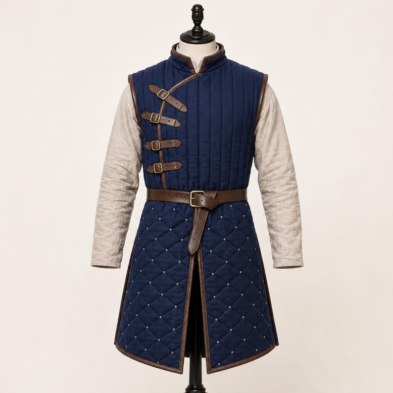 May include: A navy blue quilted vest featuring a high collar, brown leather trim, and four side-fastening buckles. The lower section displays a diamond-stitched pattern with small silver studs, secured at the waist by a brown leather belt.