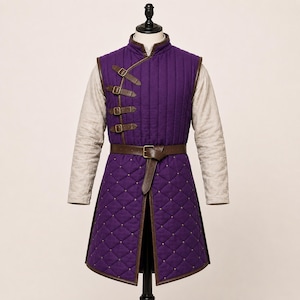 May include: A purple quilted vest with a high collar and long beige sleeves. The vest features vertical stitching on the chest, a diamond-quilted skirt, brown leather trim, four side-buckle closures, and a brown leather waist belt with a buckle.