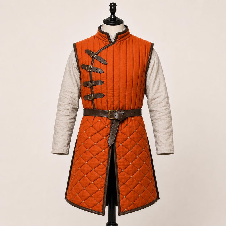 May include: A sleeveless orange quilted tunic featuring a high collar and a light-coloured long-sleeve shirt underneath. The tunic has a vertical row of four brown leather straps with metal buckles on the chest and a brown leather waist belt.