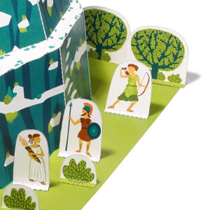 Puede incluir: Un conjunto de papercraft que presenta un castillo verde y blanco con una escena de bosque. El castillo tiene un techo blanco y paredes verdes con un borde blanco. La escena del bosque incluye &aacute;rboles verdes y un camino blanco. Tambi&eacute;n hay tres figuras en la escena: una mujer con un arco y una flecha, una mujer con un bast&oacute;n y una mujer con una espada.