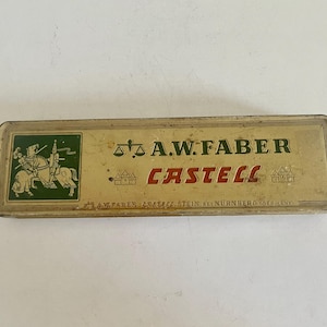 May include: A rectangular, vintage metal pencil tin with a cream-colored finish. The lid features a green square with a knight on horseback, the text A.W. FABER CASTELL, a scale icon, and the text A.W. FABER, STEIN BEI N&Uuml;RNBERG, GERMANY.