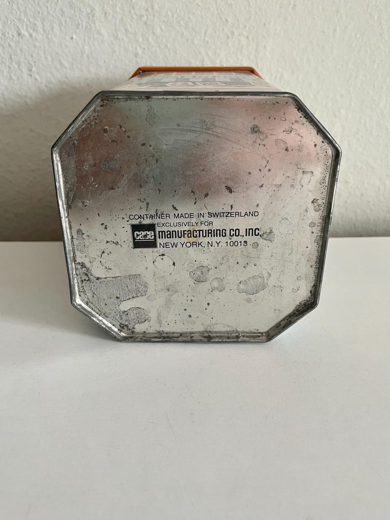 Peut inclure: Un r&eacute;cipient m&eacute;tallique vintage avec une base octogonale. Le r&eacute;cipient a une finition argent&eacute;e avec des signes d'usure. Le texte "CONTAINER MADE IN SWITZERLAND EXCLUSIVELY FOR CAME MANUFACTURING CO., INC NEW YORK, N.Y. 10013" est imprim&eacute; sur la base.