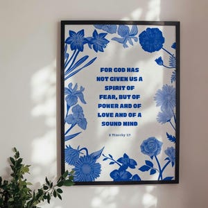 Può includere: Stampa incorniciata con una citazione in testo blu: "PERCHÉ DIO NON CI HA DATO UNO SPIRITO DI PAURA, MA DI POTENZA, DI AMORE E DI MENTE SANA." La stampa è circondata da illustrazioni floreali blu. Il testo "2 Timoteo 1:7" è in basso.