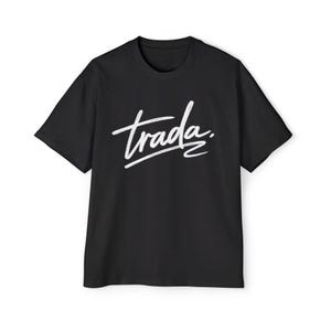 May include: Black t-shirt with the word "trada" in white script across the chest. The text is slightly slanted and underlined. The shirt has short sleeves and a crew neck.