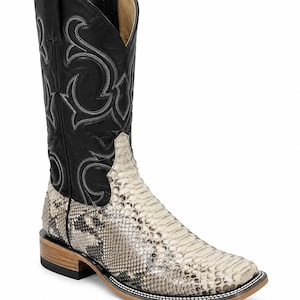 Pode incluir: Uma bota de estilo western com cano de couro preto com costuras decorativas cinzentas e pé de couro texturizado com padrão de pele de cobra em creme e cinzento. A bota tem biqueira quadrada, salto de madeira empilhada e sola preta.