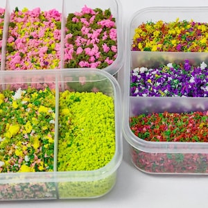 May include: Two clear plastic containers divided into sections, filled with various colors of miniature flocking material for dioramas. The contents include textures in shades of pink, green, yellow, purple, and red, resembling ground cover.