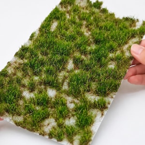 May include: A rectangular sheet of artificial grass featuring dense, vibrant green blades of varying lengths and textures. The grass is attached to a thin, light-coloured backing material, creating a realistic, tufted appearance for miniature landscapes.