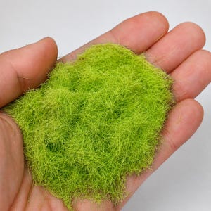 Può includere: Un ciuffo di erba statica verde lime brillante progettato per diorami di modelli. Il materiale è costituito da sottili fibre sintetiche verticali che imitano l'aspetto di un'erba da prato corta e vibrante, fornendo una superficie strutturata.