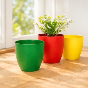 May include: Three brightly coloured plant pots in green, red, and yellow. The red pot contains white and yellow flowers. The pots are cylindrical with a textured finish, suitable for indoor or outdoor use. They sit on a wooden surface.