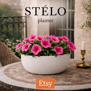 Może przedstawiać: Biała, miskowata doniczka wypełniona żywymi różowymi kwiatami petunii. Tekst STÉLO planter jest wyświetlany nad kwiatami, a pomarańczowe logo Etsy znajduje się na dole pośrodku obrazu.