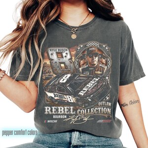 K&ouml;nnte beinhalten: Dunkelgraues T-Shirt mit einem Rennwagen-Motiv, der Nummer 8 und dem Text "REBEL COLLECTION BOURBON". Das Shirt enth&auml;lt auch den Text "KYLE BUSCH" und "NASCAR".