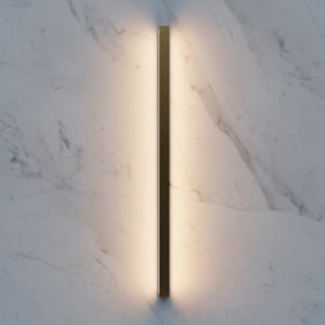 May include: A vertical wall light with a warm, diffused glow. The fitting has a dark, metallic frame and is mounted on a white marble wall. The light is evenly distributed along the length of the sconce, which is approximately 120 cm in length.