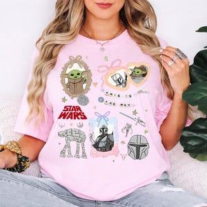 Może przedstawiać: Jasnor&oacute;żowa koszulka z grafiką Star Wars, w tym Grogu, Mandalorianinem i napisem "This is the Way". Projekt zawiera oprawione obrazy i inne elementy Star Wars.