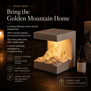 Puede incluir: Una lámpara de cúpula gris con un paisaje montañoso esculpido iluminado desde el interior. El texto dice "Bring the Golden Mountain Home". Incluye una botella de aceite esencial. Cuenta con 3 tonos de luz y un difusor de aroma.