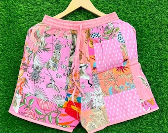 Puede incluir: Pantalones cortos de patchwork en color rosa con una variedad de patrones estampados que incluyen motivos florales, ilustraciones de animales y formas geométricas. Tienen una cintura elástica con cordón rosa a juego y un colgador de madera.
