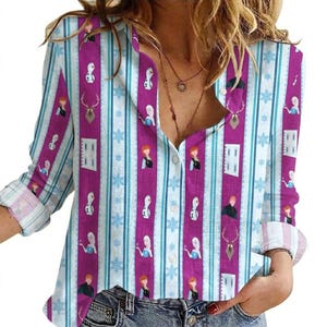 May include: A button-down shirt with a vertical striped pattern in white, light blue, and purple. The shirt features illustrations of characters, snowflakes, and deer. The long-sleeved shirt has rolled-up cuffs.