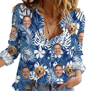 Op de afbeelding: Een blauw overhemd met een tropisch bloemenpatroon in wit en verschillende blauwtinten. De blouse heeft meerdere afbeeldingen van een lachende persoon en golden retrievers. De blouse is gemaakt van een lichte stof.
