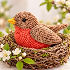 May include: A handcrafted crochet bird figurine featuring a brown head and wings, a bright orange chest, and a yellow beak. The bird is nestled inside a woven twig nest decorated with small white flowers and green leaves, creating a detailed display.
