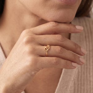 K&ouml;nnte beinhalten: Ein goldener Ring mit einem filigranen, durchbrochenen Design am Ringband. Der Blickfang besteht aus zwei miteinander verbundenen, abgerundeten, organischen Formen, die horizontal auf dem Finger liegen und ein flie&szlig;endes, poliertes Aussehen erzeugen.