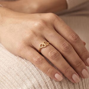 K&ouml;nnte beinhalten: Ein goldener Ring mit zwei miteinander verbundenen Buchstaben, B und C, die ein durchgehendes Design bilden. Der Ring ist d&uuml;nn und poliert und weist eine metallische Oberfl&auml;che auf, die auf dem Finger aufliegt. Die Buchstaben sind schlicht.