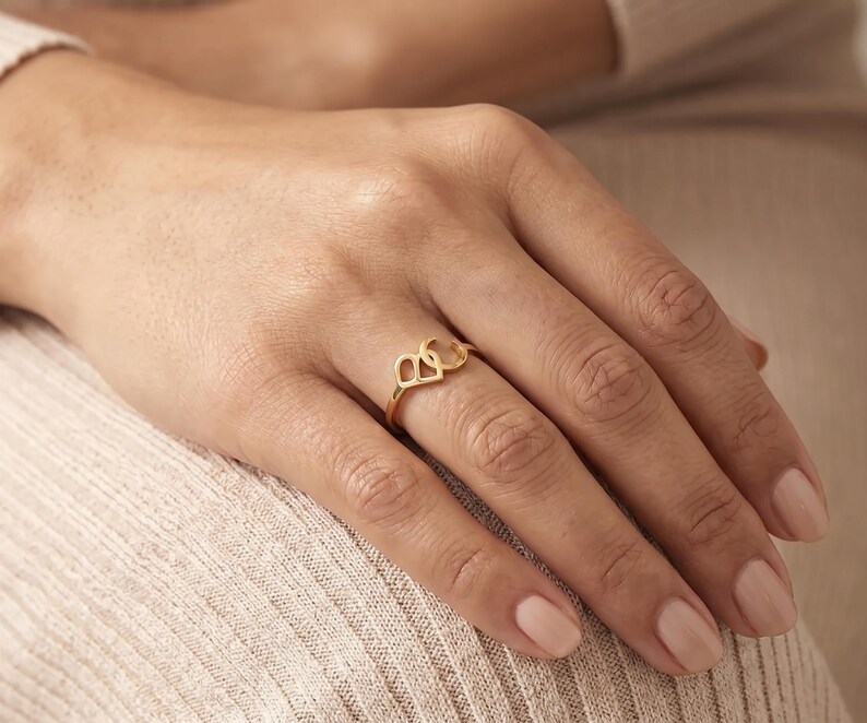 K&ouml;nnte beinhalten: Ein goldener Ring mit zwei miteinander verbundenen Buchstaben, B und C, die ein durchgehendes Design bilden. Der Ring ist d&uuml;nn und poliert und weist eine metallische Oberfl&auml;che auf, die auf dem Finger aufliegt. Die Buchstaben sind schlicht.