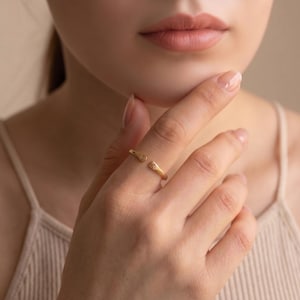 May include: A gold-toned open ring featuring two small, flat, rounded ends. Each end is engraved with a single letter, specifically the characters S and T, positioned on the finger to display the initials clearly in a simple, polished metal finish.