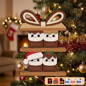 Puede incluir: Un adorno navideño de madera con un diseño de s'mores. El adorno tiene dos capas con personajes de malvavisco y chocolate sonrientes. La capa inferior tiene dos personajes que llevan un gorro de Papá Noel y un gorro de pudín navideño. El adorno está colgado de un árbol de Navidad.