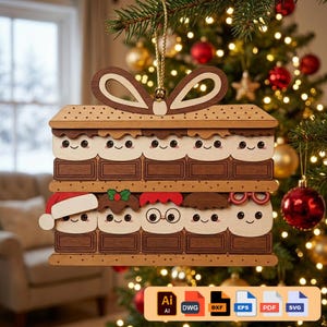 Puede incluir: Adorno navideño de madera con forma de s'more, con caras de malvavisco sonrientes y barras de chocolate. El adorno tiene un lazo en la parte superior para colgar y está decorado con un gorro de Papá Noel, acebo y gafas. El fondo es un árbol de Navidad.