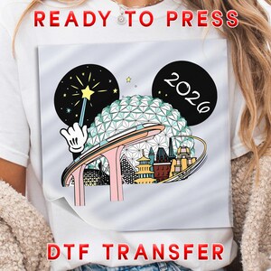 May include: White t-shirt with a colorful DTF transfer design. The design features Mickey Mouse ears, a wand, and the year 2026. The words "READY TO PRESS" and "DTF TRANSFER" are printed in red.