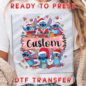 May include: A DTF transfer featuring a festive design with several blue cartoon characters wearing Santa hats and holding gifts. The word "Custom" is displayed on a pink banner. The words "READY TO PRESS" and "DTF TRANSFER" are also visible.
