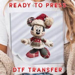 May include: A white t-shirt featuring a DTF transfer graphic of a cartoon mouse character wearing a red and beige plaid Christmas hat with a pom-pom, a matching plaid dress, and shoes. The text READY TO PRESS DTF TRANSFER is printed in red.