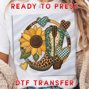 May include: A white t-shirt featuring a DTF transfer graphic of a cowboy boot with a leopard print foot and teal floral shaft, a large yellow sunflower, and several patterned hearts arranged in a circular design with the text READY TO PRESS.