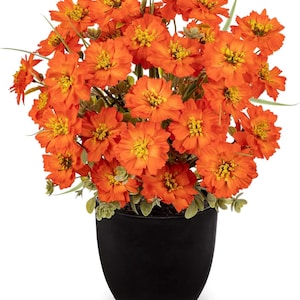 May include: A vibrant arrangement of orange flowers with yellow centers, set in a sleek, black, oval-shaped pot. The artificial flowers have green foliage and are a decorative accent for home or office.