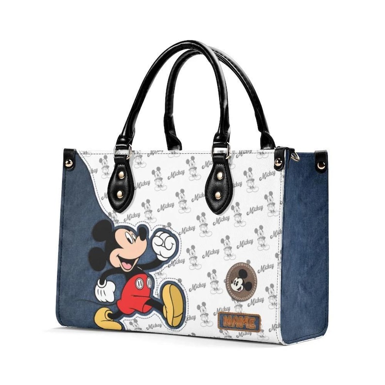 May include: White tote bag featuring a Mickey Mouse design. The bag has black handles and accents, with a denim-like blue side panel. The main body is patterned with Mickey Mouse silhouettes and the word "Mickey".