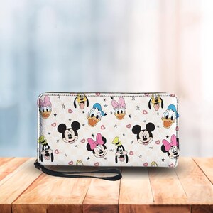 Puede incluir: Cartera blanca con un patr&oacute;n repetido de caras de Mickey Mouse, Minnie Mouse, Donald Duck, Daisy Duck y Goofy. La cartera tiene una correa de mu&ntilde;eca negra y un cierre de cremallera. Peque&ntilde;os corazones y estrellas dispersos.