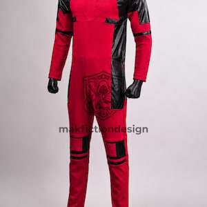 Puede incluir: Un mono de cuerpo entero rojo y negro con mangas largas, cuello alto y paneles negros en hombros, costados y rodillas. La prenda muestra un logotipo oscuro de una figura encapuchada y el texto makfictiondesign en la parte frontal del torso.