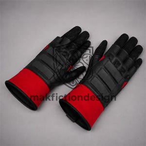 Puede incluir: Un par de guantes negros y rojos con nudillos acolchados, paneles texturizados en los dedos y un puño ancho rojo. Los guantes muestran el texto makfictiondesign en el centro. El diseño incluye secciones reforzadas en el dorso de la mano.