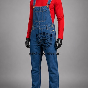 Puede incluir: Un peto de mezclilla azul con un bolsillo en el peto y botones de metal, usado sobre una camisa roja de manga larga. Un logotipo gr&aacute;fico negro que muestra una figura encapuchada y el texto makfictiondesign est&aacute; impreso en la tela vaquera.