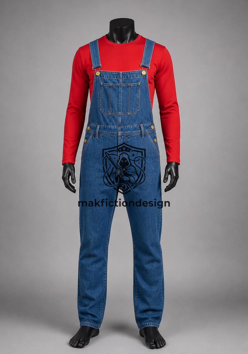 Puede incluir: Una camiseta roja de manga larga bajo un peto vaquero azul con botones dorados y un bolsillo en el pecho. En la parte delantera hay un gr&aacute;fico negro de una figura encapuchada dentro de un escudo junto al texto makfictiondesign.