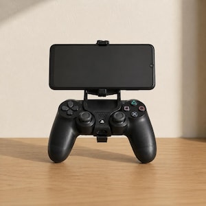 Puede incluir: Un mando de juego negro con un soporte para smartphone montado en la parte superior. El mando cuenta con una cruceta, dos joysticks analógicos y cuatro botones de acción con símbolos de triángulo, círculo, cruz y cuadrado en colores.