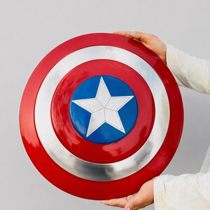 May include: A circular shield featuring a glossy red outer ring, a metallic silver middle ring, and a vibrant blue center circle. A large, five-pointed white star is centered within the blue circle, creating a bold, iconic, and symmetrical design.