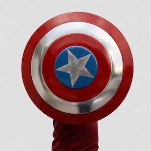 May include: A circular shield featuring a concentric design with a bright red outer ring, a metallic silver middle ring, and a blue center circle containing a large, five-pointed silver star. The shield has a smooth, reflective finish.
