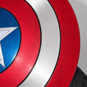 May include: A circular shield featuring a concentric design with a metallic silver outer ring, a vibrant red middle band, and a deep blue center. A large, five-pointed silver star is centered within the blue circle, with thin black lines separating the colors.
