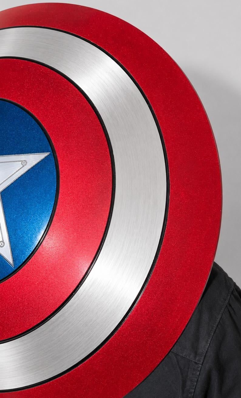 May include: A circular shield featuring a concentric design with a metallic silver outer ring, a vibrant red middle band, and a deep blue center. A large, five-pointed silver star is centered within the blue circle, with thin black lines separating the colors.