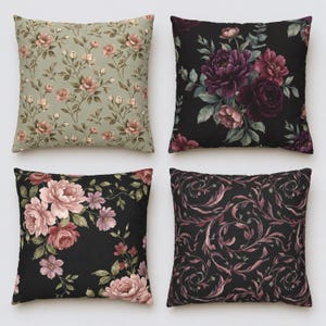 May include: Four square throw pillows featuring distinct floral and botanical patterns. The top left pillow has a sage green background with small pink roses. The other three pillows feature dark black backgrounds with large purple, pink, and mauve floral arrangements or swirling vine motifs.