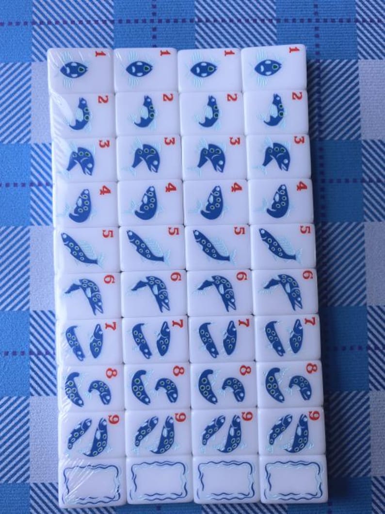 Nature-inspired American mahjong tile set with glossy white acrylic tiles featuring blue fish dot tiles, green bamboo designs, coral-inspired crack tiles, illustrated wildflower flower tiles, and colorful animal joker tiles. Modern engraved NMJL-style mahjong set arranged in clean flat lays with minimalist styling and outdoor mountain aesthetic, photographed on a soft white background with premium collectible game design.