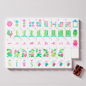Könnte beinhalten: Ein Satz weißer Mahjong-Steine mit farbenfrohen Illustrationen und Symbolen. Die Steine zeigen florale Designs, Bambus und chinesische Schriftzeichen. Das Set enthält Steine mit den Wörtern "NEWS" und "Joker". Ein Schildpatt-Stein ist ebenfalls vorhanden.