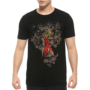 Może przedstawiać: Czarny t-shirt z krótkim rękawem z nadrukiem graficznym przedstawiającym postać Hellboya w kolorze czerwonym, umieszczonym pod stylizowanym, złotym i brązowym wzorem kwiatowo-szkieletowym, który rozciąga się na klatce piersiowej odzieży.