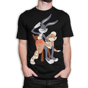 May include: A black short-sleeved t-shirt featuring a graphic print of Bugs Bunny and Lola Bunny. Bugs Bunny is depicted standing behind Lola Bunny, who is bent over a wooden chair. The graphic has a distressed, vintage-style texture.